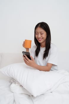 Smiling young asian woman using smart phone in bedroom at home. lifestyle, woman lying on bed.