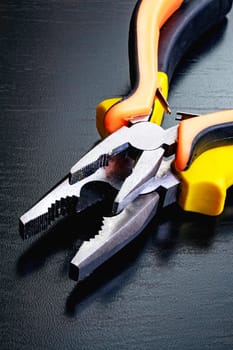 Two pliers, tools on a black wooden table close up