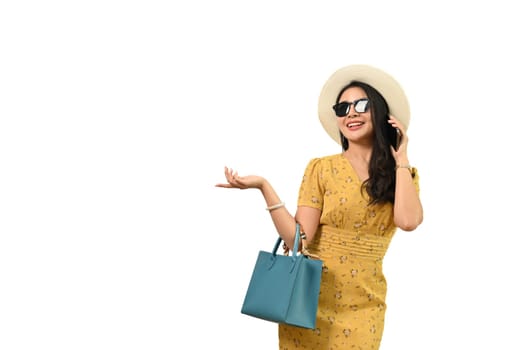 Cheerful Asian woman dressed in summer clothes and sunglasses standing on white background, enjoying summer vacation concept.