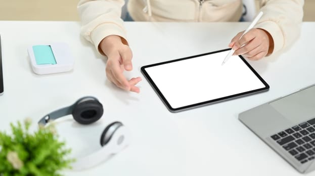 Cropped image of young woman making research, browsing internet via digital tablet at working desk.