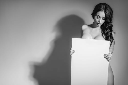 Sexy naked brunette woman holding empty board. attractive girl with blank board with copy space. black and white