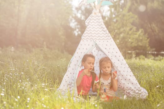 Two happy laughing little girls in camping tent in dandelion field.