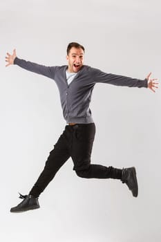 Photo of cheerful young man dressed in black t-shirt jumping over white background looking at camera.