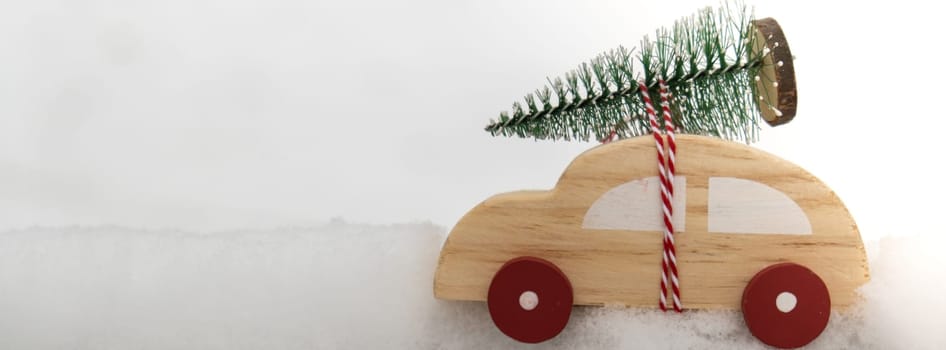 Wooden car carrying Christmas tree over snow. Copy space for text Toy car in snowy landscape. Merry Christmas and Happy New Year concept. Winter is coming Greeting card