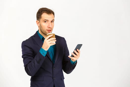 Portrait of a smiling young business man using smartphone and holding cup of coffee isolated on a white background