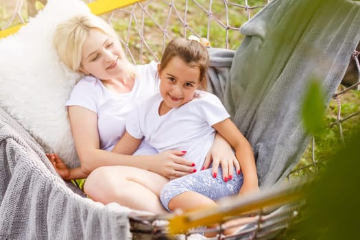 loving family spends time together in summer time enjoy the little things. slow life. mom and little daughter relax in a hammock in the summer in the garden.