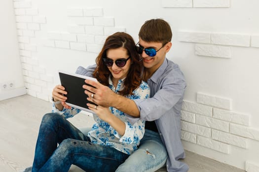 Simple happiness. Cheerful lovely couple cuddling on sofa at home, using digital tablet for websurfing, free space.