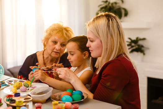Little girl and her grandmother painting Easter eggs at home