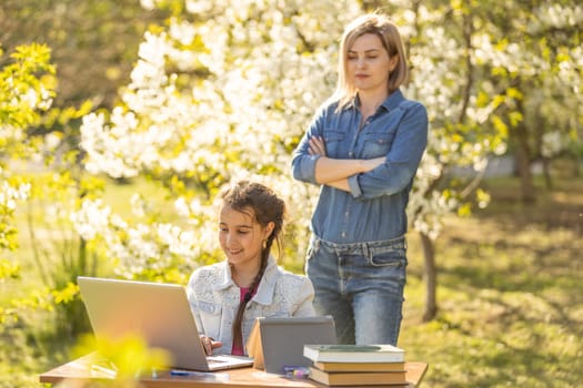 Beautiful mom with little daughter resting with a laptop in the park on a sunny day. Study, Learning, harmony, happiness, paradise - concept.