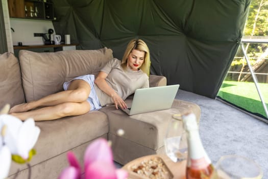 Happy young woman chatting online by using laptop in dome camping. Glamping vacation concept.