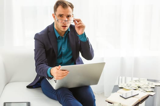 Multitasking. Handsome young man wearing glasses and working with touchpad while sitting on the couch in office