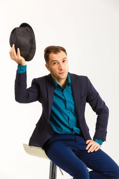 sexy confident man wearing a black tuxedo sitting on a metal chair on light background,