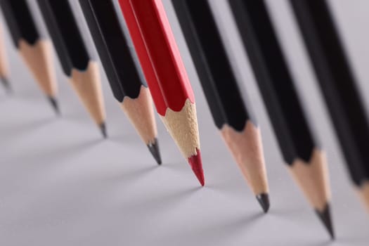 Sharp red pencil stands out from identical black pencils on gray background. Independent thinking special and business success concept