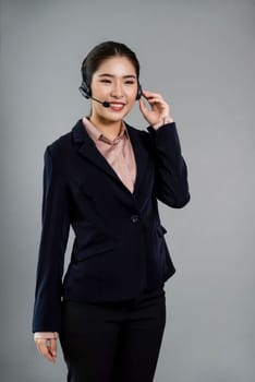 Attractive asian female call center operator with happy smile face advertises job opportunity on empty space, wearing a formal suit and headset on customizable isolated background. Enthusiastic