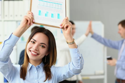 Portrait of smiling beautiful businesswoman holding clipboard with financial charts in background successful team. Successful business deal and partnership