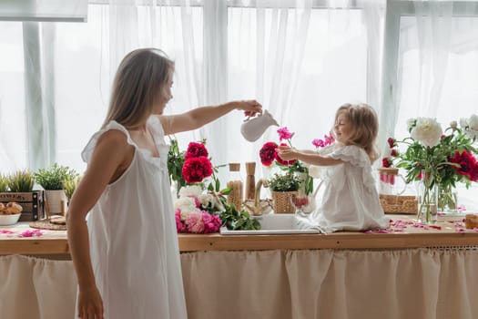 A little blonde girl with her mom on a kitchen countertop decorated with peonies. The concept of the relationship between mother and daughter. Spring atmosphere