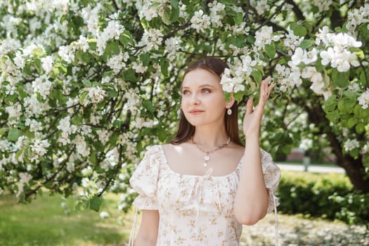 An attractive long-haired woman walks in the spring in the park of blooming apple trees. Spring portrait of a woman