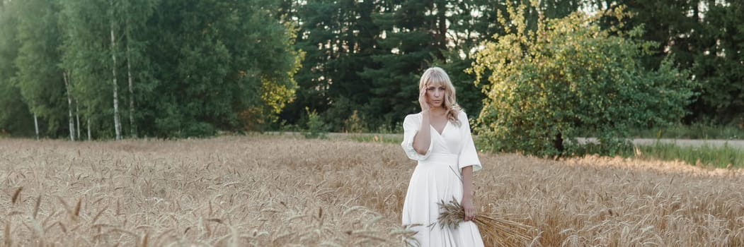 A blonde woman in a long white dress walks in a wheat field. The concept of a wedding and walking in nature.