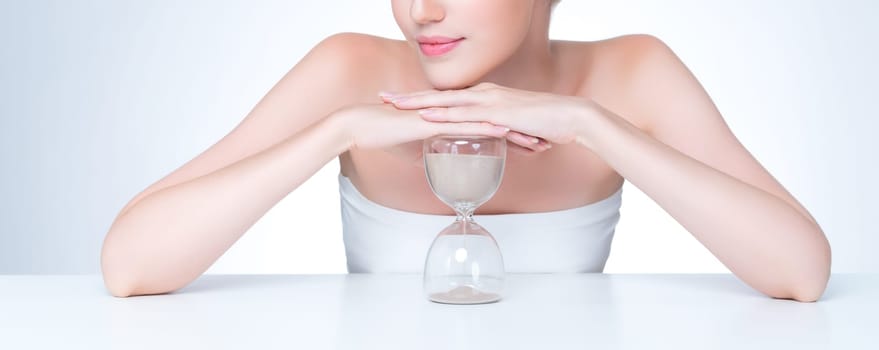 Closeup personable model holding hourglass in beauty concept of anti-aging skincare treatment. Young girl portrait with perfect smooth clean skin and flawless soft makeup in isolated background