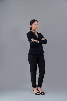 Full body length image of confident young businesswoman stands on isolated background, posing in formal black suit. Office lady or manager with smart and professional appearance. Enthusiastic