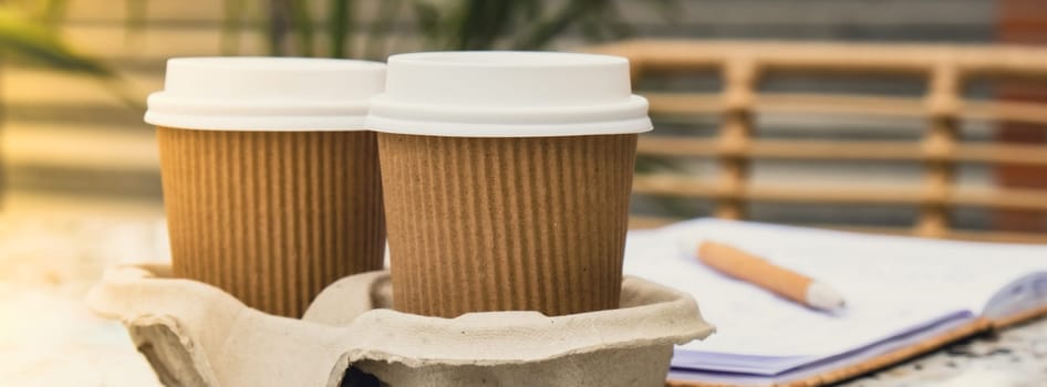 Two paper cups with lid for tea to go. Coffee take away on the table. Take-out coffees with brown paper cup holder. Brown safety cardboard collars. Take away box for cups. Cardboard tray