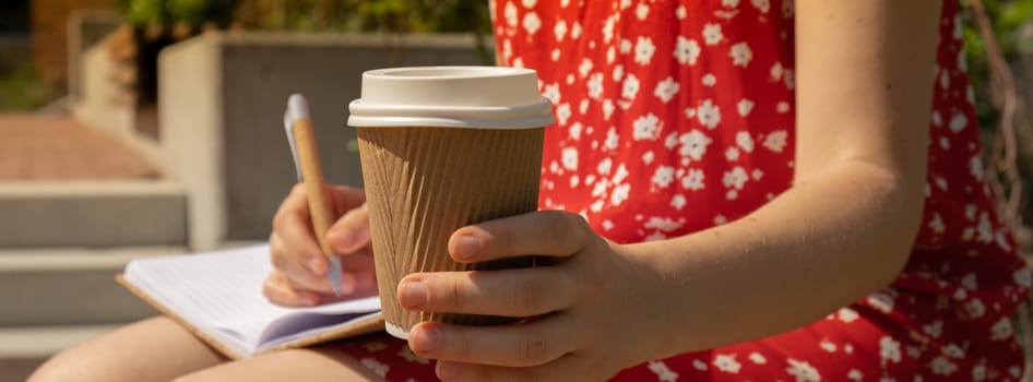 Unrecognizable Young woman in red dress drinking coffee from craft paper cup Writing Gratitude Journal on wooden bench. Today I am grateful for. Self discovery journal, self reflection creative writing, self growth personal development concept. Self care wellbeing spiritual health, being mindful, holistic health practices habits mindfulness