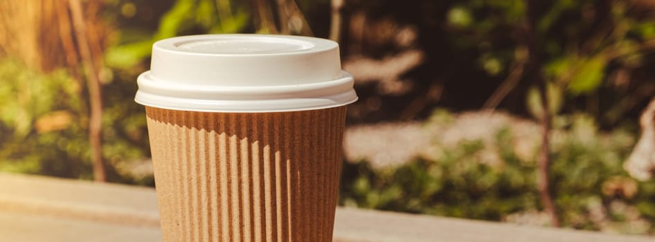 Eco recycling paper cup with coffee or tea on kraft paper on wooden table. Breakfast on the street in the park on bench. Take away coffee to go. Copy space for text. Disposable Cardboard coffee outdoors