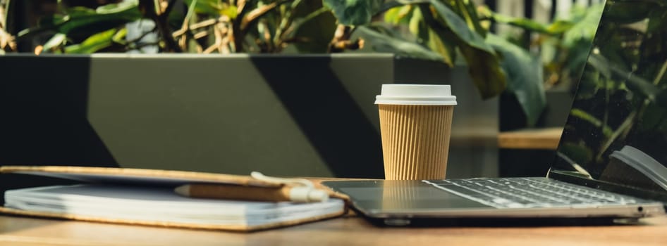 Mock up of modern laptop at table in co-working space. Remote Freelancer's place of work. Study and work online. Remote business education. Concept of webinar. E-learning Workstation Take away recycling coffee from paper cup. Coffee break Technology in Life Copy space