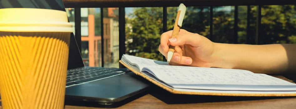 Unrecognizable Young woman study at wooden table in shopping mall food court. Drinking coffee from paper cup. Student making homework Female hands writing on notebook gratitude journal self reflection self discovery in Co-Working Space. Goals, to-do list in the modern office building