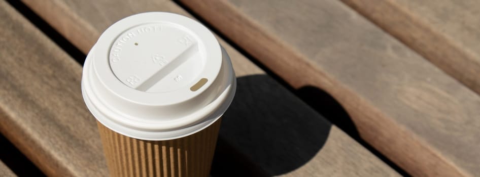 Eco recycling paper cup with coffee or tea on kraft paper on wooden table. Breakfast on the street in the park on bench. Take away coffee to go. Copy space for text. Disposable Cardboard coffee outdoors