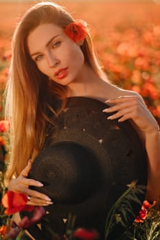 naked girl with a black hat in her hands in a poppy field at sunset.