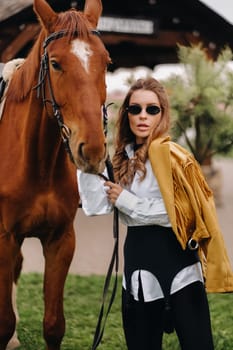 Stylish girl with glasses stands next to a horse on the street.