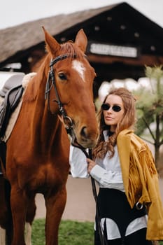 Stylish girl with glasses stands next to a horse on the street.