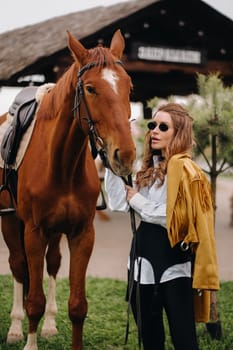 Stylish girl with glasses stands next to a horse on the street.