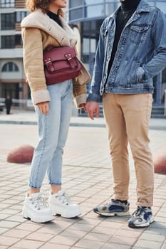 Cheerful couple in casual warm clothes have a walk outdoors in the city near business building.