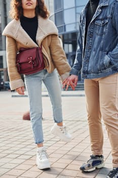 Cheerful couple in casual warm clothes have a walk outdoors in the city near business building.