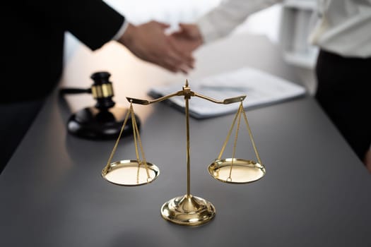 Focus gavel and justice scale on blur background of lawyer colleagues handshake after successful legal deal for lawsuit to advocate resolves dispute in court ensuring trustworthy partner. Equilibrium