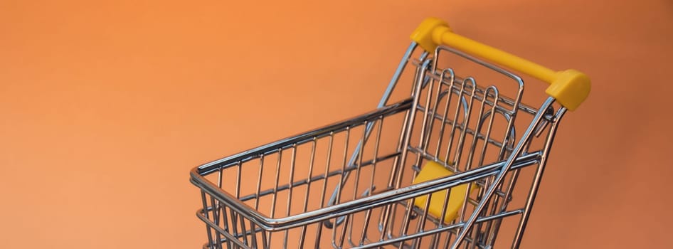 Empty shopping trolley cart on beige background. Copy space for your text. Online shopping, buy mall market shop consumer concept. Small toy supermarket grocery push cart. Food crisis. Rising food cost, grocery prices shortage mass hunger. Inflation