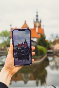 Female traveler in historical places courtyard of landmark and shoots short video on phone. Tourist photographs historic place on sunny day in Gdansk Poland. Unrecognizable woman Tourism and blogging sharing live online for audience travel together recording video on mobile phone