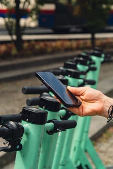 Female hand uses mobile phone to scan QR code on Electric scooter on the street on e-scooter, rental service app. Alternative transportation in city. Eco friendly transportation