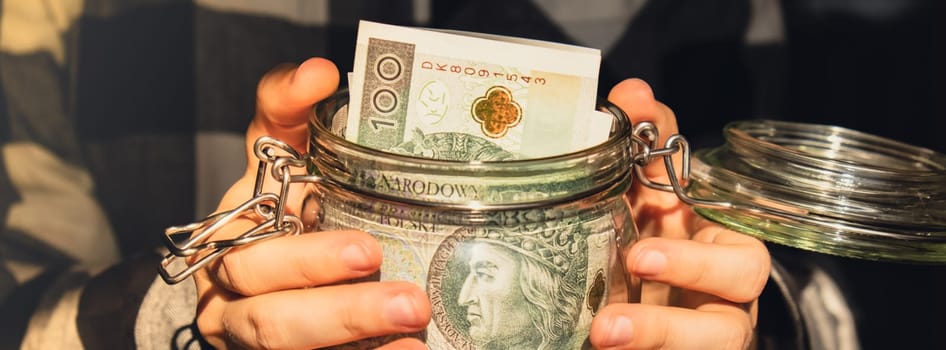 Polish zloty banknote saving money in glass jar. Unrecognizable woman moderate consumption and economy Collecting money. Tips. Business, finance, saving, banking and people concept. Extra money, passive income. Saving for travel, crisis, house, car, education, retirement Banner