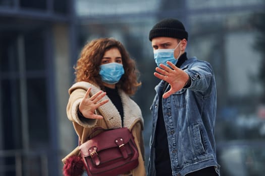 Couple in protective masks have a walk outdoors in the city near business building at quarantine time. Conception of coronavirus.