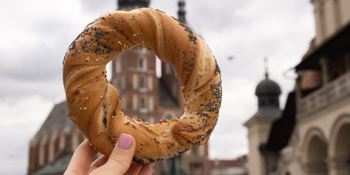 Tourist woman eating bagel obwarzanek traditional polish cuisine snack waling on Market square St. Mary's Basilica on the Krakow Main Square Rynek Glowny Poland. Krakow architecture, old city architecture. Historic Roman Catholic church in Krakow Baroque architecture Travel tourist attraction