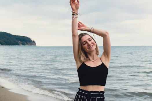 Young woman standing on blurred beachside background. Attractive female enjoying walking the sea shore. travel and active lifestyle concept. Springtime. Relaxation, youth, love, lifestyle solitude with nature. Wellness wellbeing mental health inner peace Slow life digital detox