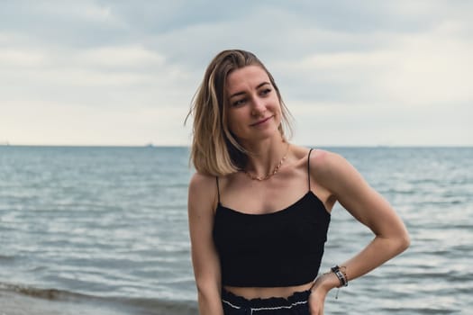 Young woman standing on blurred beachside background. Attractive female enjoying walking the sea shore. travel and active lifestyle concept. Springtime. Relaxation, youth, love, lifestyle solitude with nature. Wellness wellbeing mental health inner peace Slow life digital detox