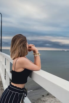 Young woman standing on wooden pier blurred beachside background. Attractive female enjoying the sea shore travel and active lifestyle concept. Springtime. Wellness wellbeing mental health inner peace Slow life digital detox