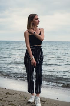 Young woman standing on blurred beachside background. Attractive female enjoying walking the sea shore. travel and active lifestyle concept. Springtime. Relaxation, youth, love, lifestyle solitude with nature. Wellness wellbeing mental health inner peace Slow life digital detox