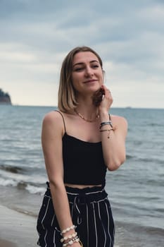 Young woman standing on blurred beachside background. Attractive female enjoying walking the sea shore. travel and active lifestyle concept. Springtime. Relaxation, youth, love, lifestyle solitude with nature. Wellness wellbeing mental health inner peace Slow life digital detox