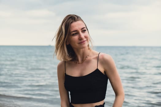 Young woman standing on blurred beachside background. Attractive female enjoying walking the sea shore. travel and active lifestyle concept. Springtime. Relaxation, youth, love, lifestyle solitude with nature. Wellness wellbeing mental health inner peace Slow life digital detox