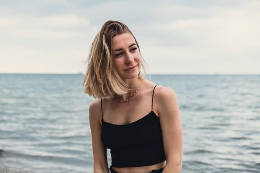 Young woman standing on blurred beachside background. Attractive female enjoying walking the sea shore. travel and active lifestyle concept. Springtime. Relaxation, youth, love, lifestyle solitude with nature. Wellness wellbeing mental health inner peace Slow life digital detox